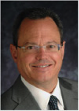 A man in suit and glasses smiling for the camera.